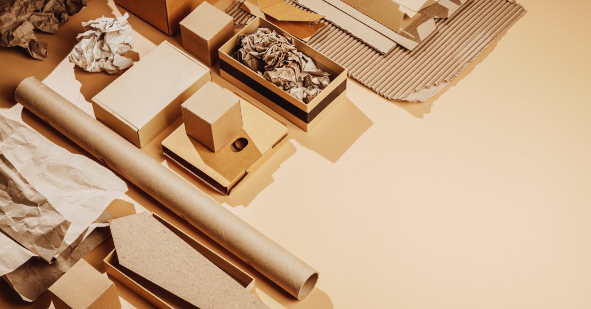 An assortment of cardboard boxes, crumpled paper, corrugated sheets, and a roll of paper arranged on a tan surface.