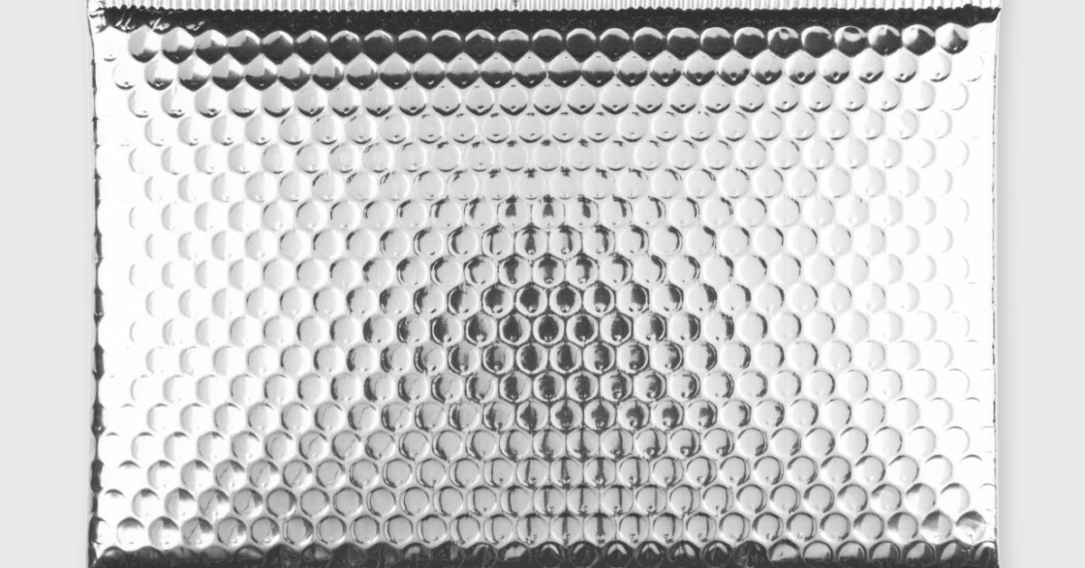 A shiny silver bubble mailer lies on a white background, with a sealed edge and a reflective, crinkled surface.