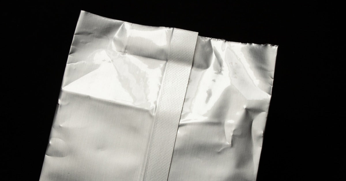 A close-up of gray thermal packaging with a sealed edge against a black background, illuminated in studio lighting.